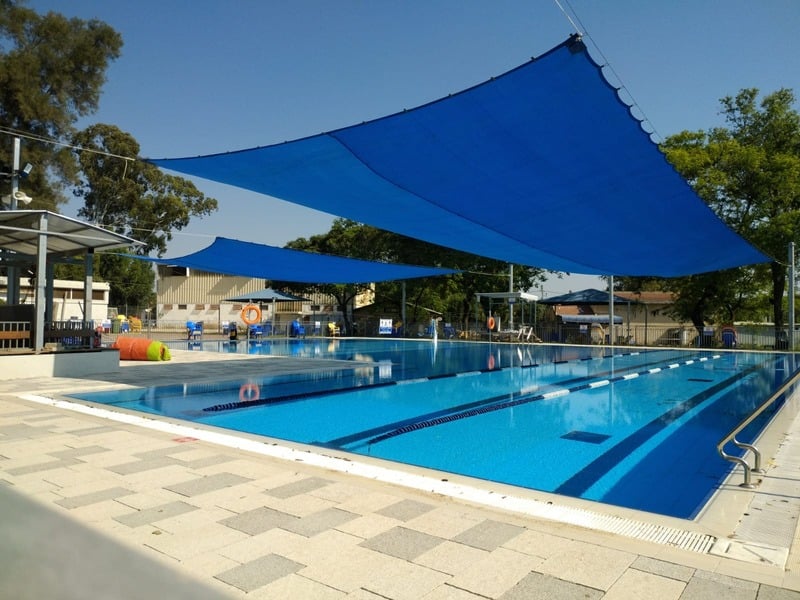 בריכת השחייה החצי אולימפית עם הצללות כחולות ומדשאות